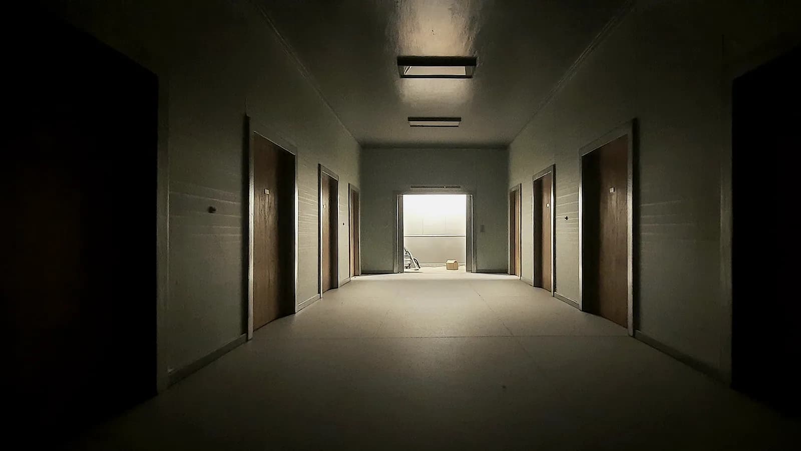 A corridor with several doors ajar, light spilling unevenly from each